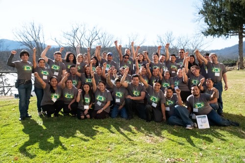 A group at the Workers' Center standing on grass in the sunlight with fists raised.