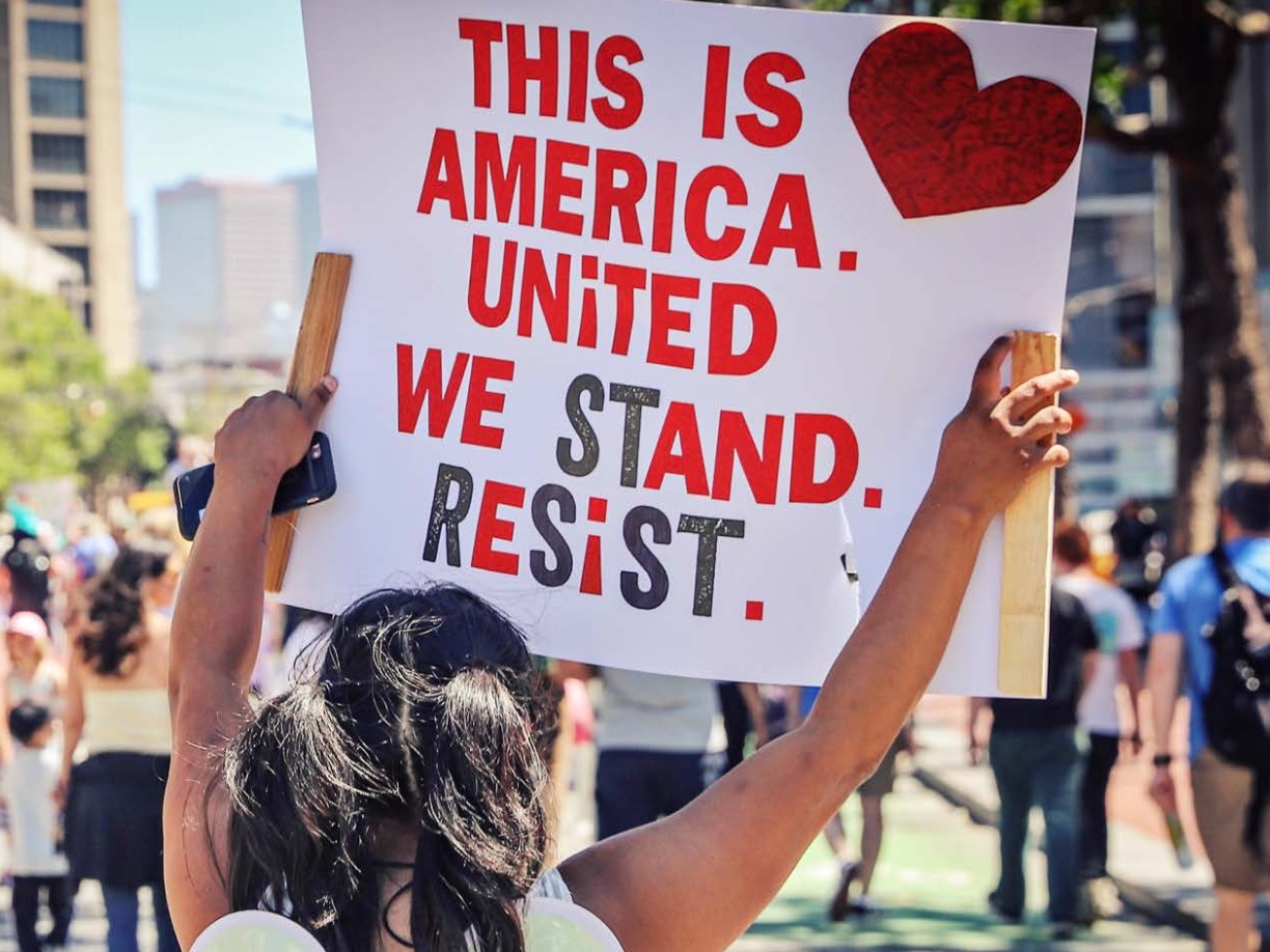 The cover of GCIR's 2019 Annual Report, Pushing Back, Looking Forward. The cover of GCIR's report, Immigration Legal Services in California: A Time for Bold Action, featuring a woman holding a sign reading, "This is America. United We Stand. Resist."