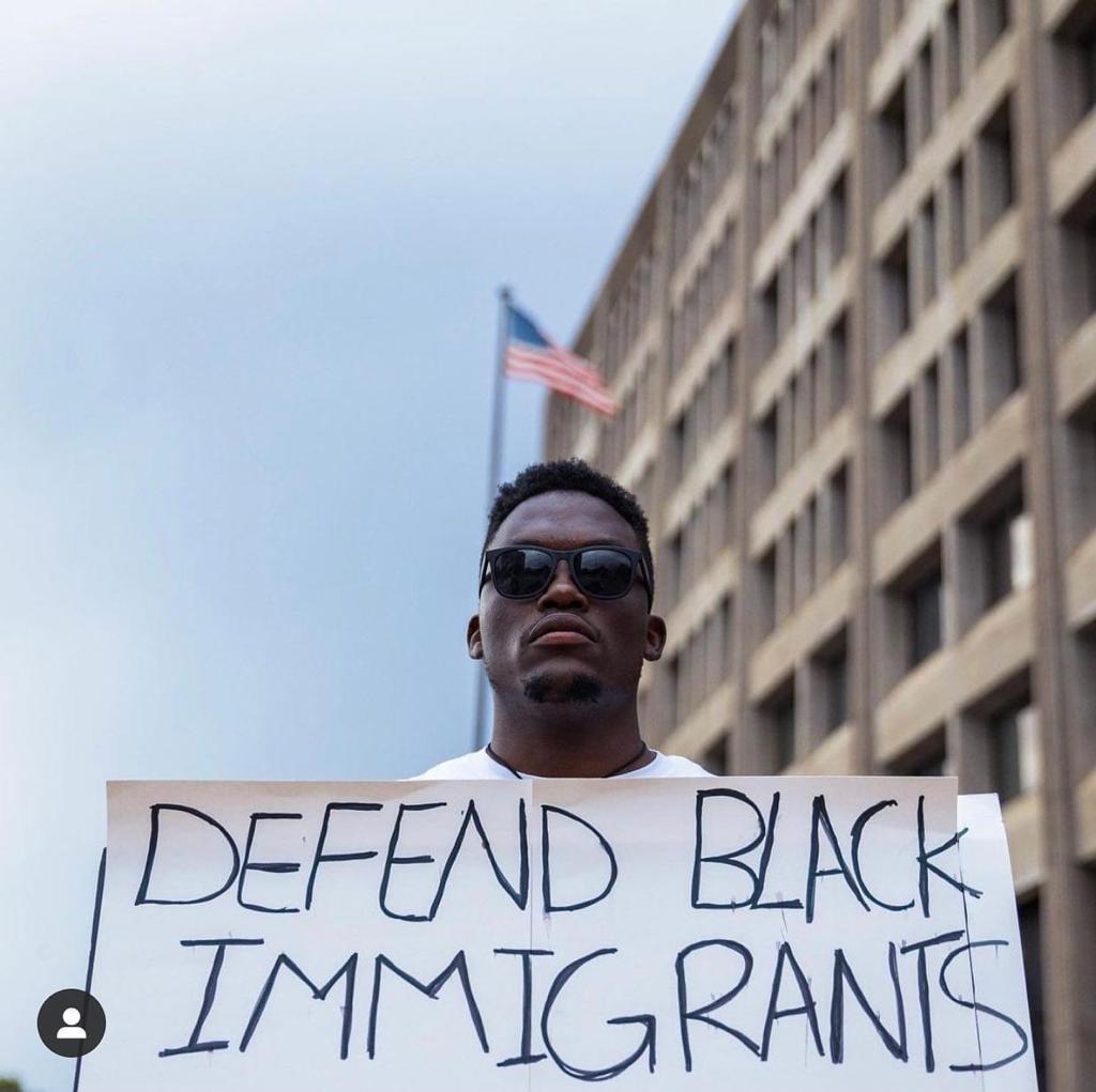 defend-black-immigrants-sign-held-by-man