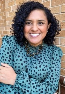 Magaly Urdiales smiles while standing against a brick wall.