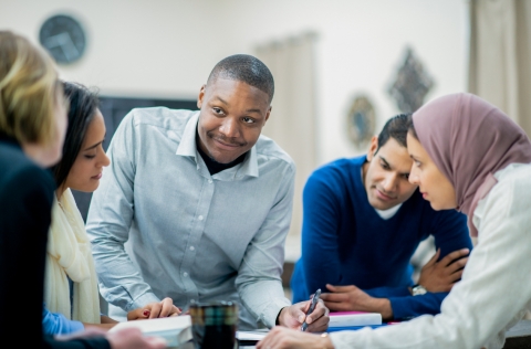 A young Black man leads a group discussion with his multi-ethnic colleagues.